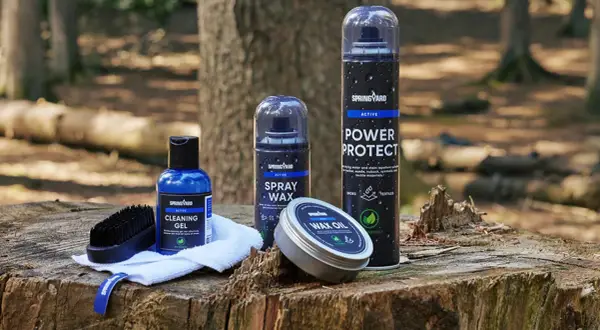 Produkter för impregnering av syntetskor: rengöringsgel, sprayvax, power protect och wax oil, placerade på en trädstubbe i skogen.