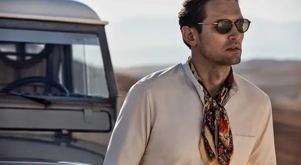 Man med solglasögon och en färgglad scarf, redo att knyta scarf för äventyr vid en gammal bil.