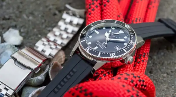Orient Star dykare med svart gummiarmband och ett extra länkarmband. Rött rep i bakgrunden.