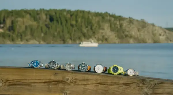 En rad olika klockor, från eleganta till sportiga, ligger uppradade på en träbrygga med en båt i bakgrunden. Varje boett klocka berättar sin egen historia.