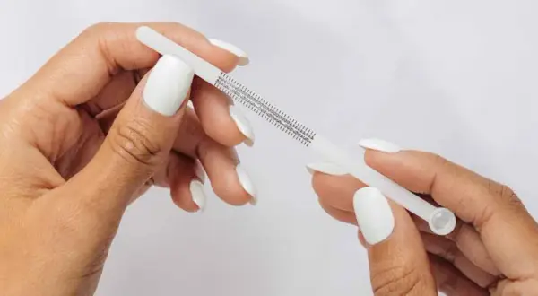 Händer med vita naglar mäter fingerstorlek med ett mätverktyg som visar ring storlek 15.