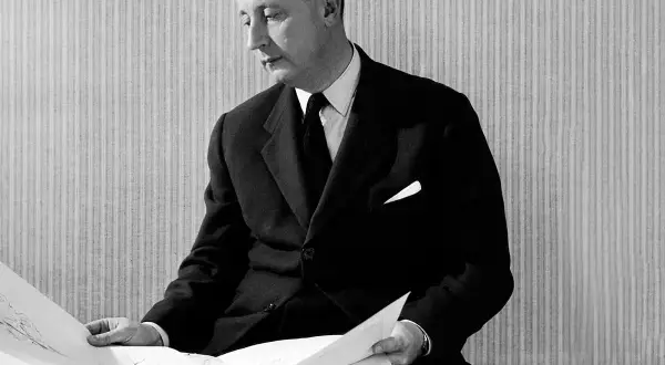 Man i kostym från mode 1950-talet granskar ritningar.