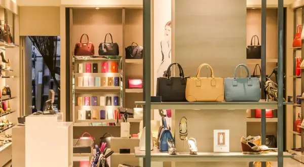 Ett skyltfönster med väskor och skor från italienska modehus. Lyxiga accessoarer visas upp i en elegant butiksmiljö.