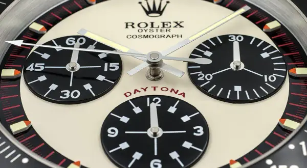 En närbild av en Rolex Daytona, en ikonisk klocka som Paul Newman själv bar. Den har tre svarta urtavlor på en krämfärgad bakgrund.