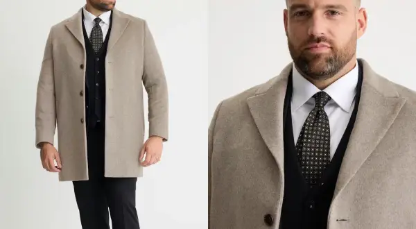 Man i beige jacka till kostym, med svart väst och mönstrad slips.