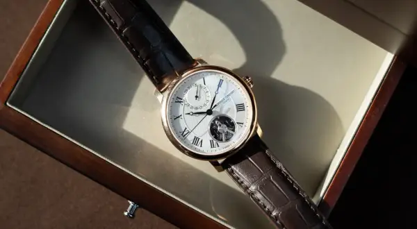 Ett elegant armbandsur med brunt läderband och ett synligt mekaniskt urverk. Klockan ligger i en träask.