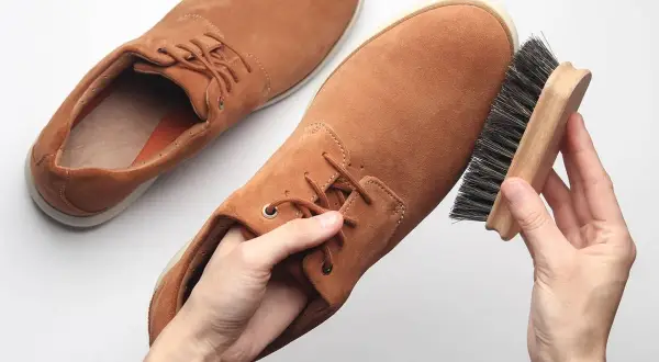 Händer borstar bruna mockaskor med en borste. För att hålla dem fina kan man behöva mocka vatten.