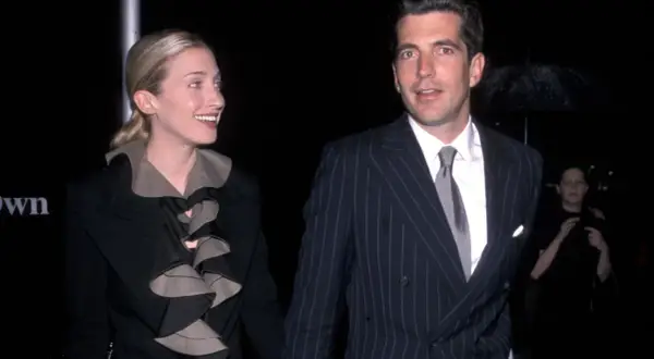 Carolyn Bessette Kennedy och John F. Kennedy Jr. på en tillställning. Hon bär en svart kavaj med volanger, han en randig kostym.