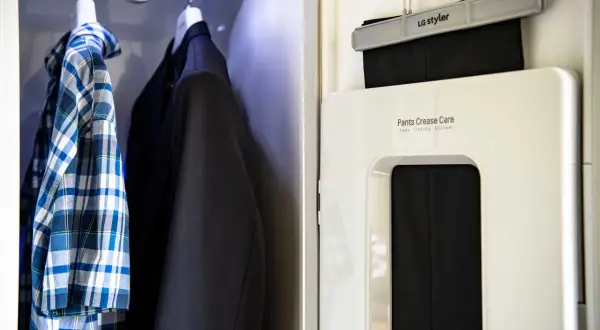 En rutig skjorta och en kavaj hänger redo. Bredvid syns en LG Styler som hjälper till att stryka skjorta med steamer och pressa byxveck.