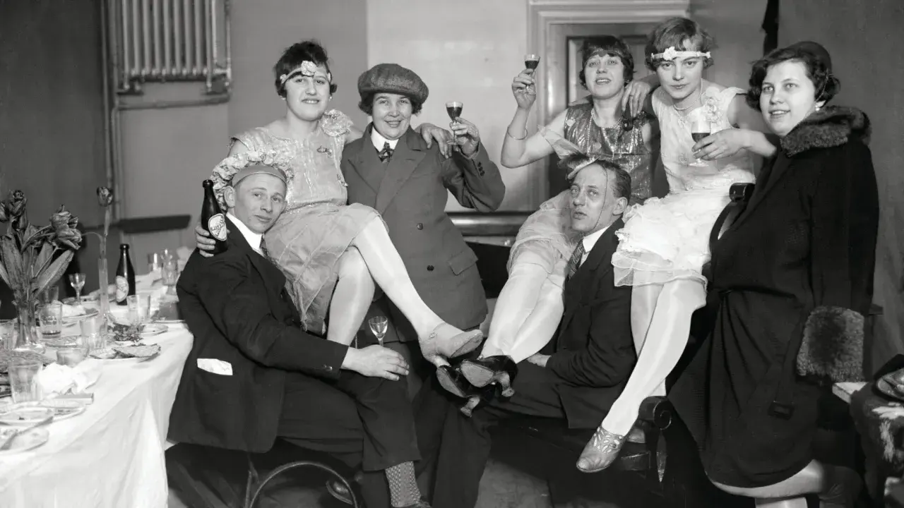 Festligt sällskap i mode 1920-tal, med kvinnor i klänningar och män i kostym, skålar och njuter av festen.