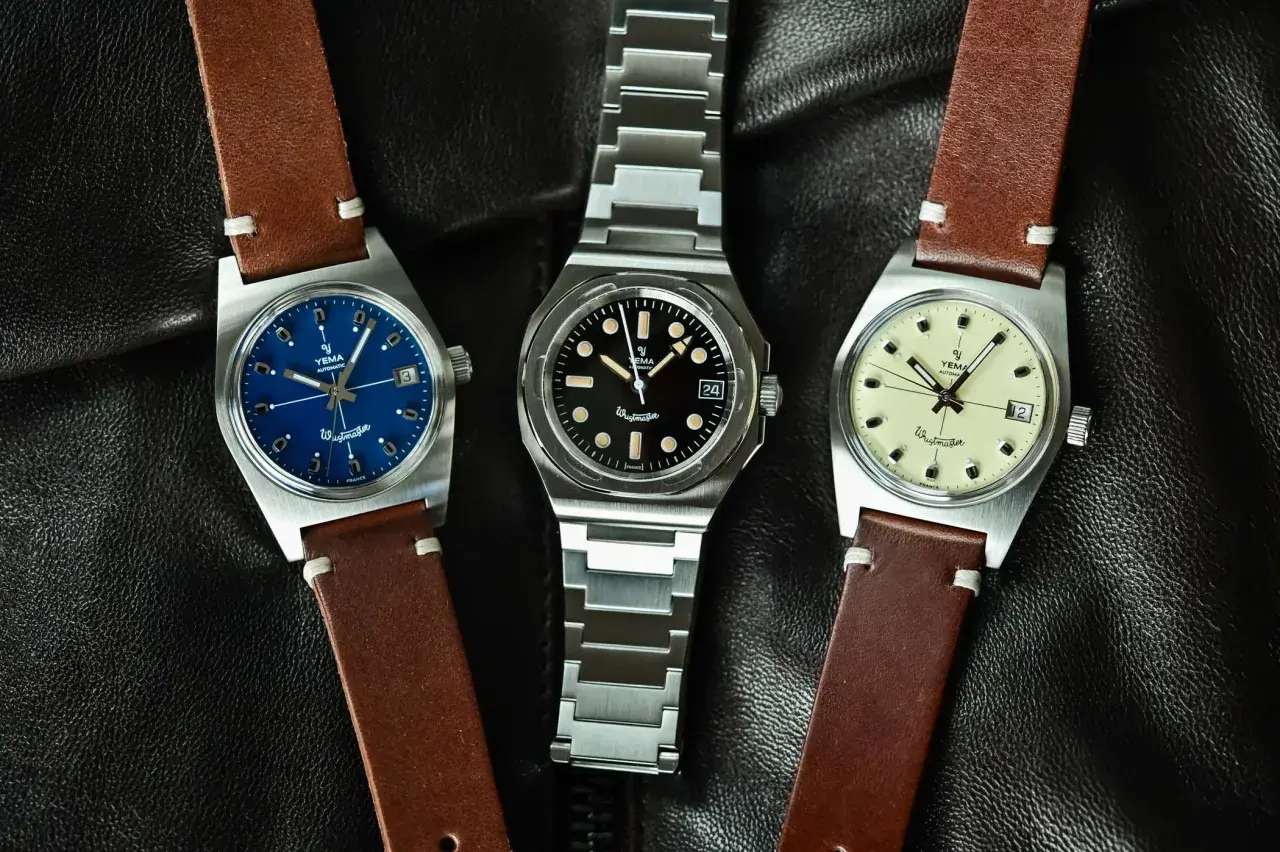 Tre Yema Wristmaster Traveller-klockor med blå, svart och krämfärgad urtavla, på en svart läderbakgrund.