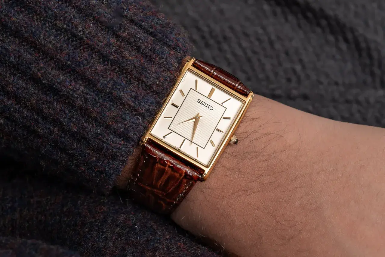 En elegant guldfärgad Seiko-klocka med brun läderrem på en arm. Dessa japanska klockor är kända för sin precision.