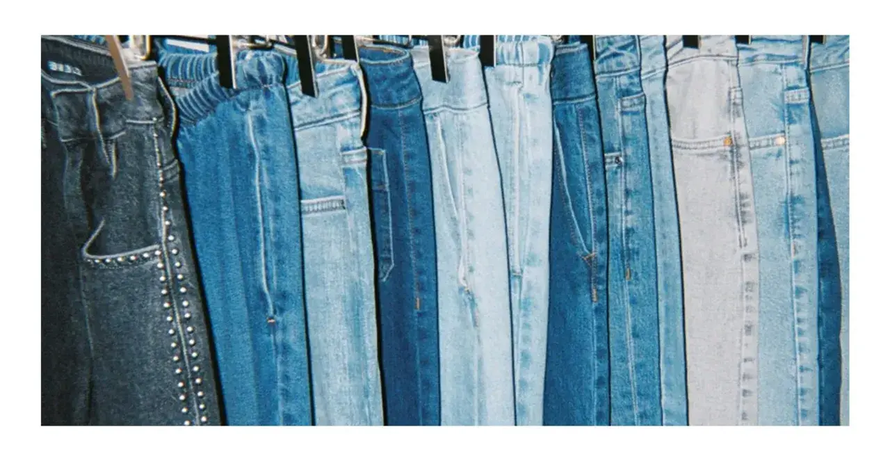 En rad blå jeans hänger på galgar, redo att stryka. Olika nyanser av denim, från mörkblått till ljusblått, skapar en visuell fest.
