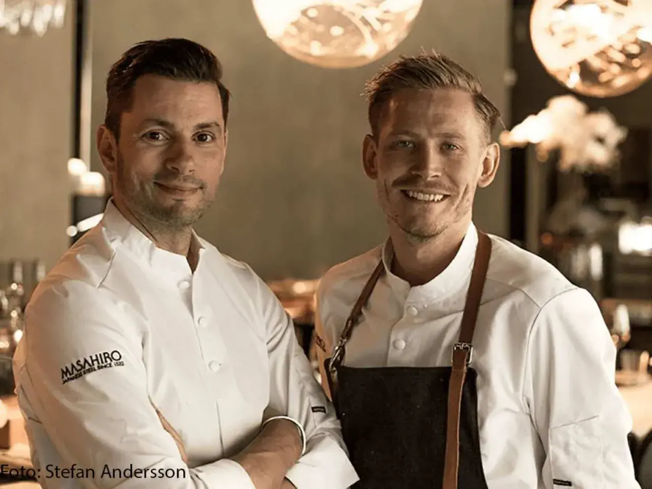 Två kockar ler mot kameran. Deras vita kockrockar och förkläden antyder en professionell miljö, kanske en restaurang som får bra allegrine recensioner.