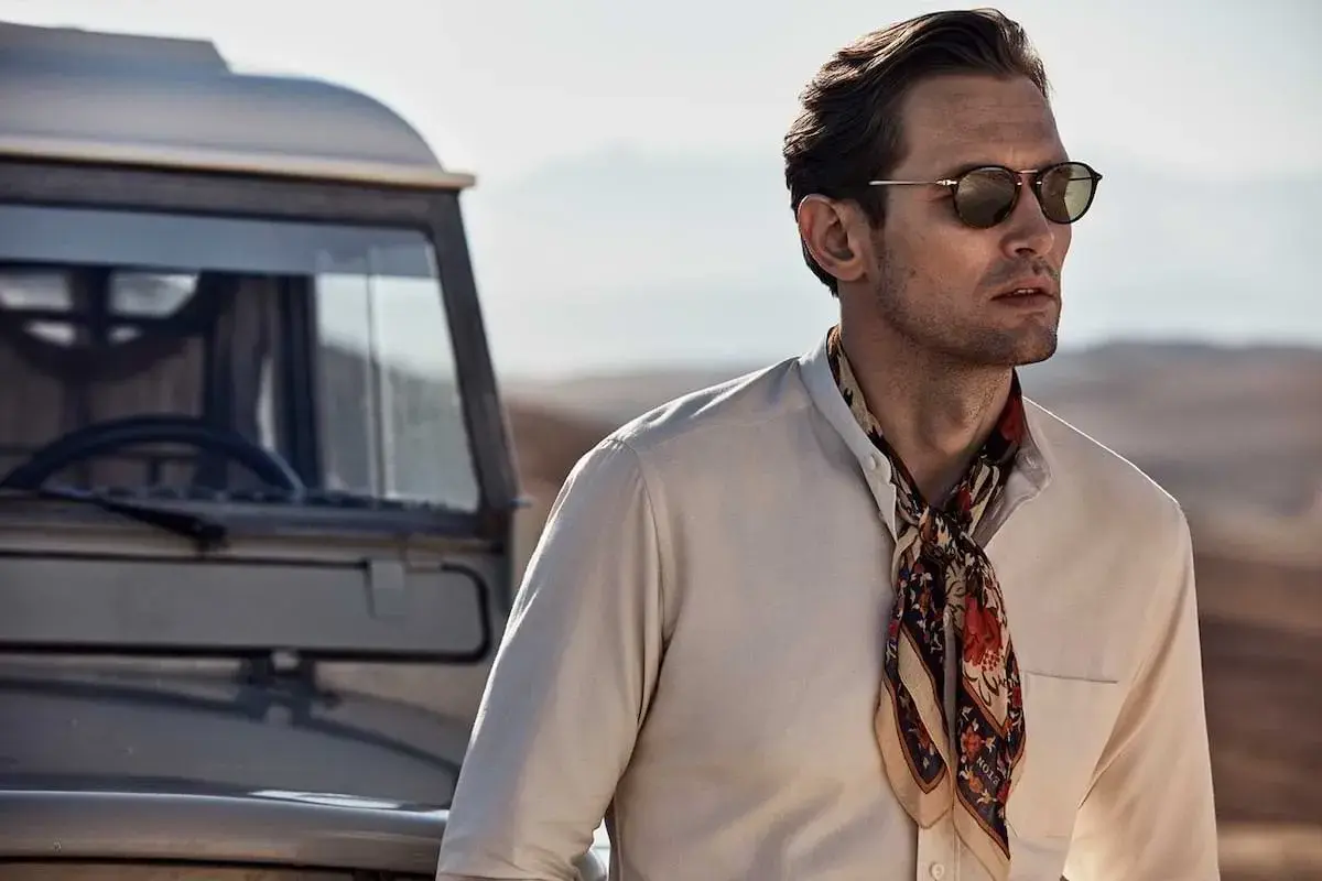 Man med solglasögon och en färgglad scarf, redo att knyta scarf för äventyr vid en gammal bil.