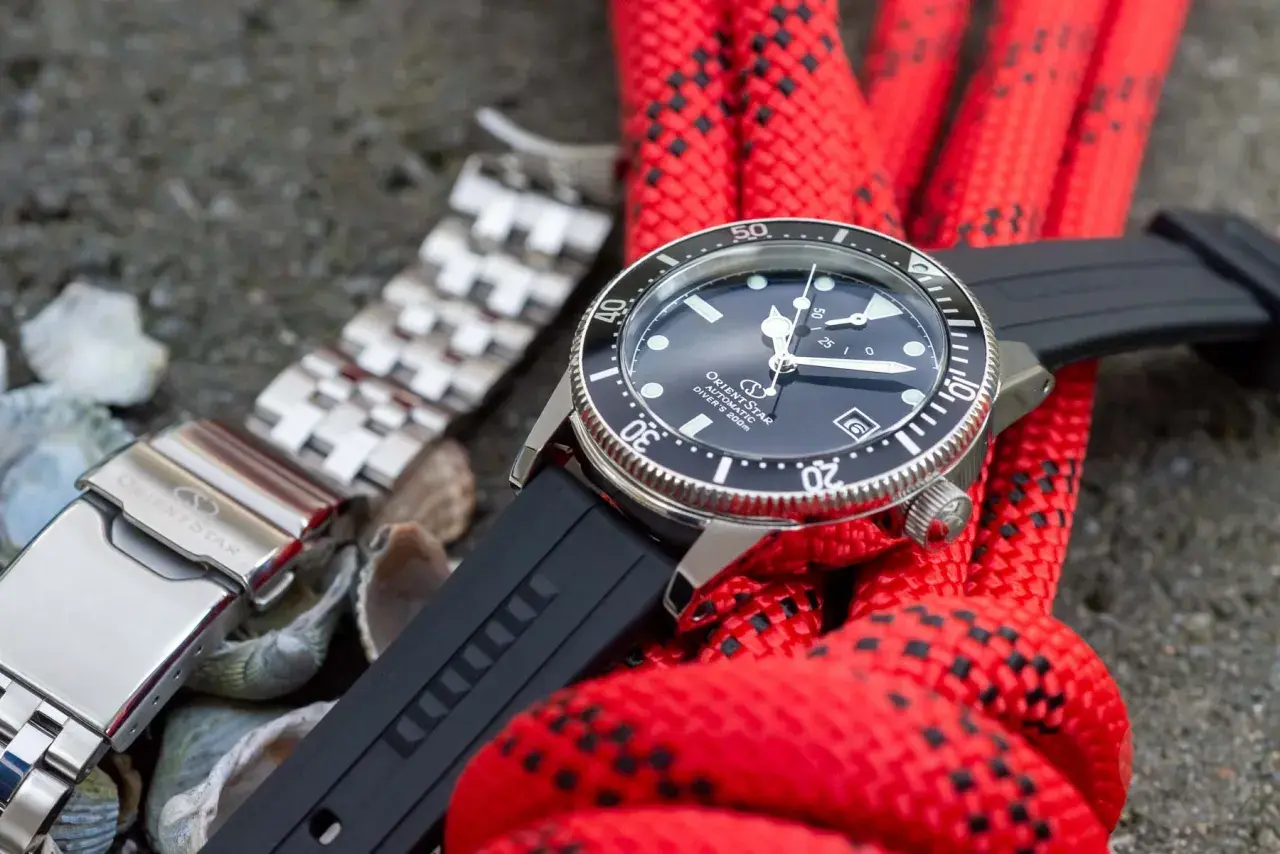 Orient Star dykare med svart gummiarmband och ett extra länkarmband. Rött rep i bakgrunden.
