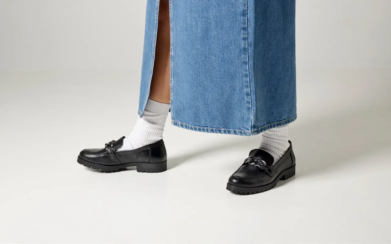 Svarta loafers med kedja och vita strumpor till dam. Perfekt för en trendig look.