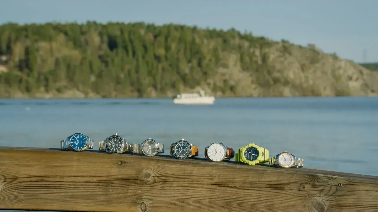 En rad olika klockor, från eleganta till sportiga, ligger uppradade på en träbrygga med en båt i bakgrunden. Varje boett klocka berättar sin egen historia.