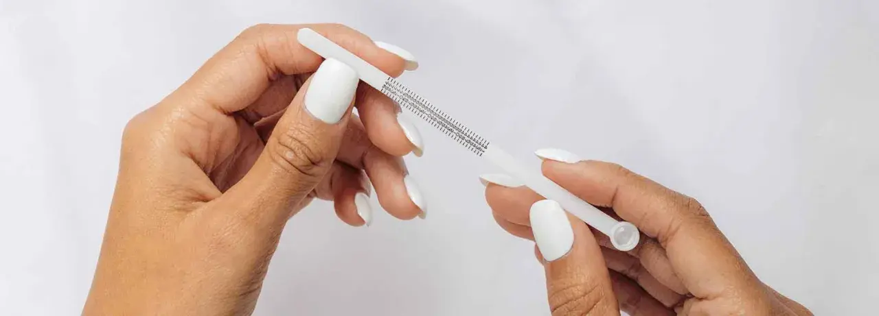 Händer med vita naglar mäter fingerstorlek med ett mätverktyg som visar ring storlek 15.