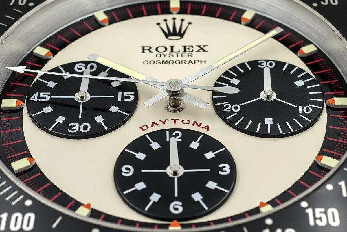 En närbild av en Rolex Daytona, en ikonisk klocka som Paul Newman själv bar. Den har tre svarta urtavlor på en krämfärgad bakgrund.