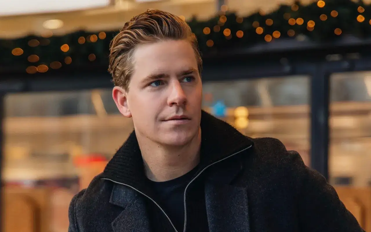 Martin Hansson i snygg h&ouml;stmode, med en m&ouml;rk rock och en stickad krage. Bakgrunden &auml;r suddig med julbelysning.