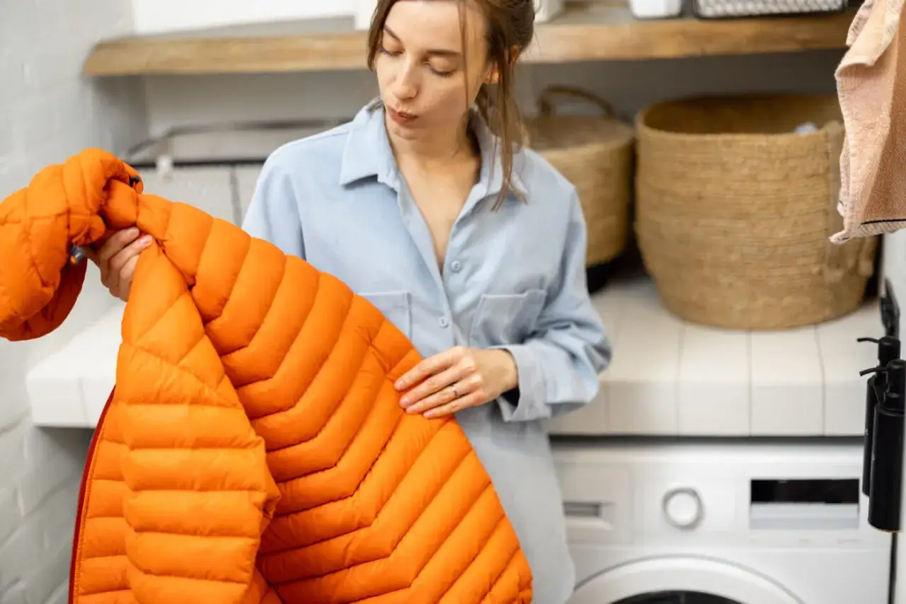 Kvinna håller en orange dunjacka, redo att torktumla den för att återställa fluffigheten.