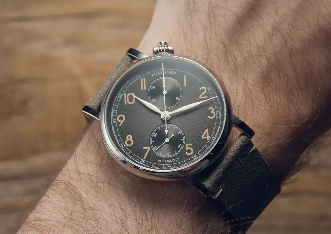 En närbild på ett Longines-ur med grå urtavla och guldfärgade siffror, monterat på en arm. Ett perfekt ur för den som vill ha koll på tiden.