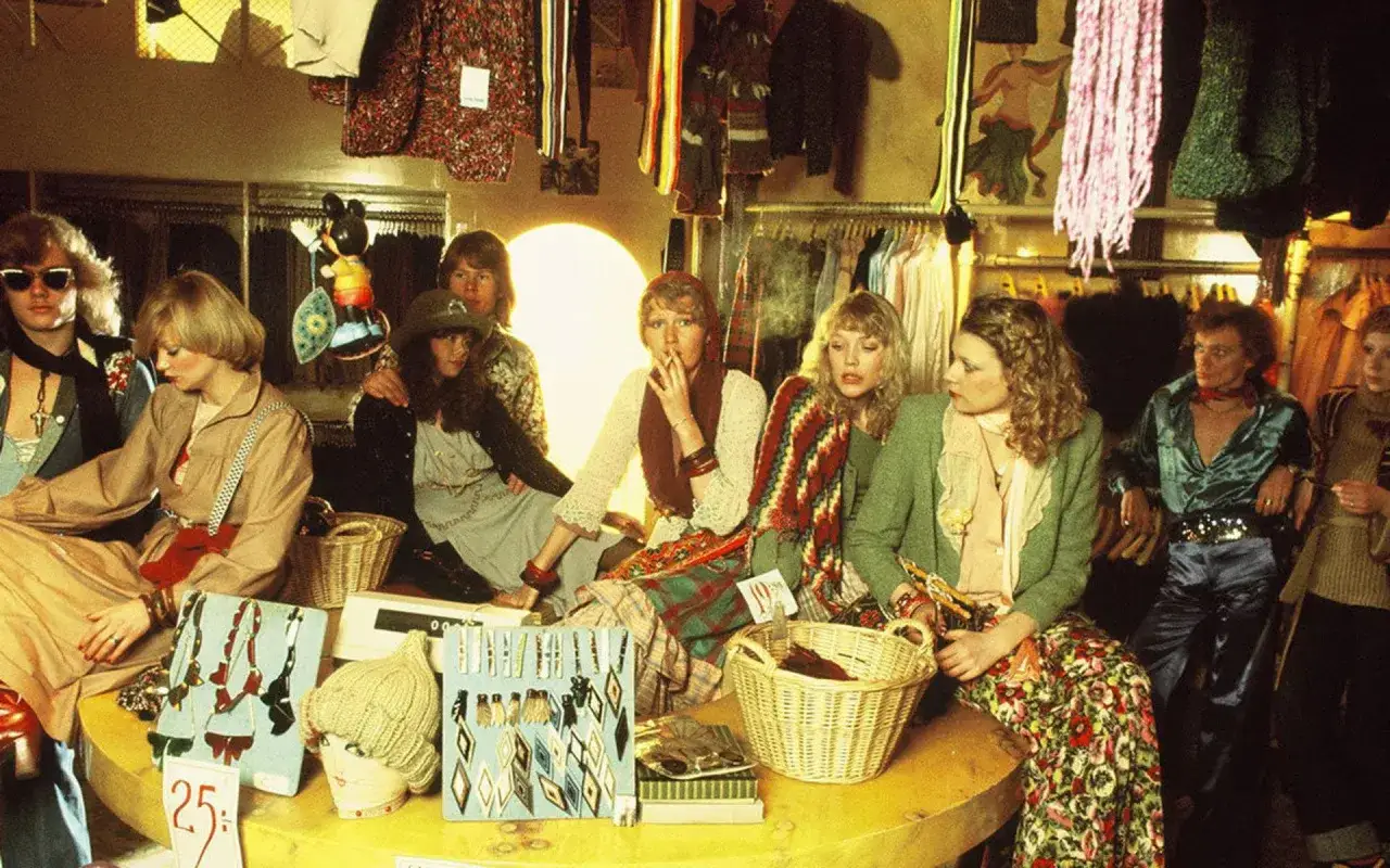 En grupp unga människor i en retrobutik. En kvinna röker, en annan har på sig jeans gul och blå.