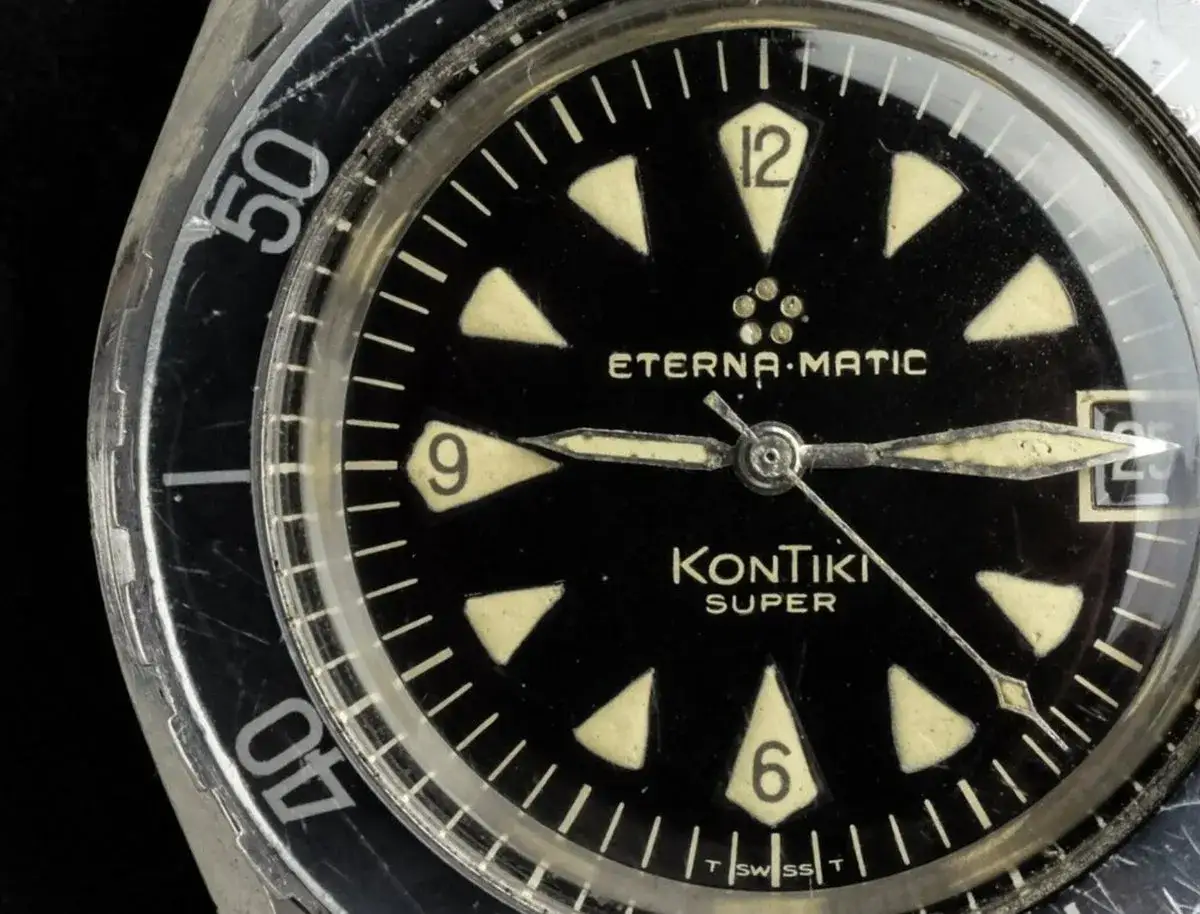En närbild av en sliten Eterna-Matic Kontiki Super dykarklocka. Den svarta urtavlan har lysande markörer och visare.