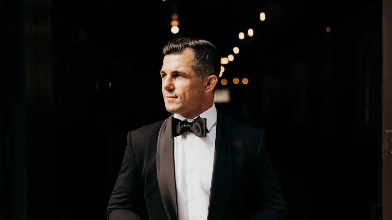 Man i smoking med fluga, redo för en kväll med black tie tema. Bakgrunden är mörk med ljusslingor.
