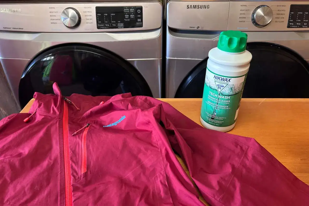 En vinröd Patagonia-jacka ligger framför en tvättmaskin och en flaska Nikwax Tech Wash, redo att impregnera jackan.