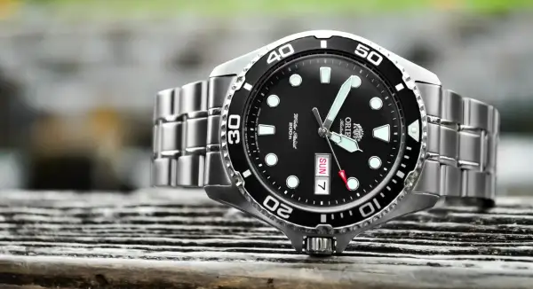 En närbild på en orient ray 2 dykarur med svart urtavla och silverfärgat armband, placerad på en träyta.