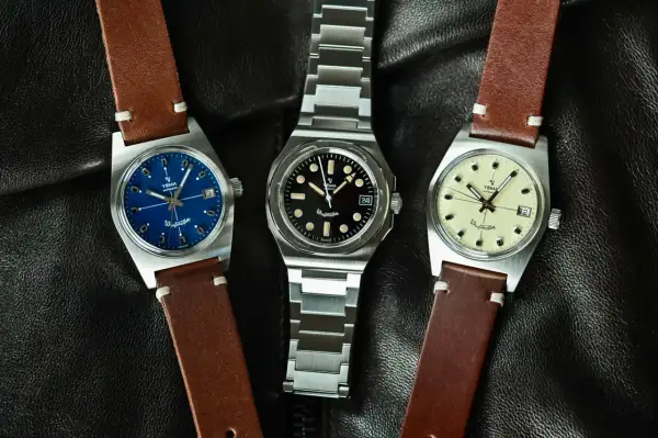 Tre Yema Wristmaster Traveller-klockor med blå, svart och krämfärgad urtavla, på en svart läderbakgrund.