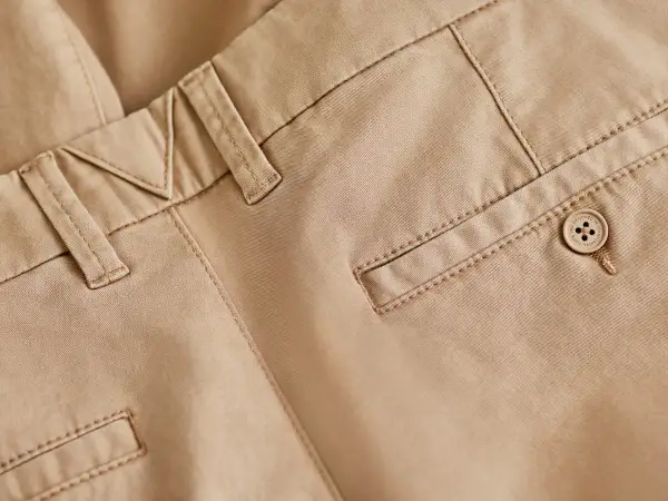 Detaljbild på beige chinos med snygga sömmar och en knapp. Perfekt bas för många olika skor till chinos.