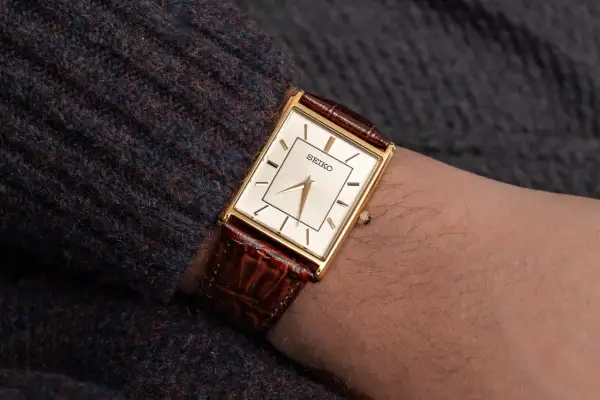 En elegant guldfärgad Seiko-klocka med brun läderrem på en arm. Dessa japanska klockor är kända för sin precision.