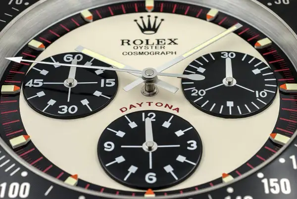En närbild av en Rolex Daytona, en ikonisk klocka som Paul Newman själv bar. Den har tre svarta urtavlor på en krämfärgad bakgrund.