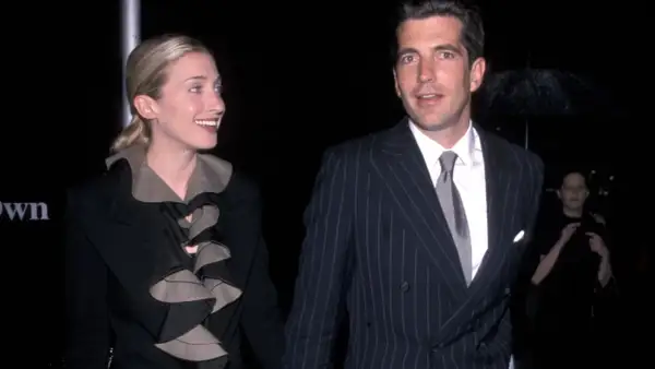 Carolyn Bessette Kennedy och John F. Kennedy Jr. på en tillställning. Hon bär en svart kavaj med volanger, han en randig kostym.