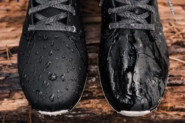 Två svarta kängor, en behandlad för att stöta bort vatten, den andra inte. Vattenpärlor på den ena, blöt på den andra. Perfekt för att spraya skor.